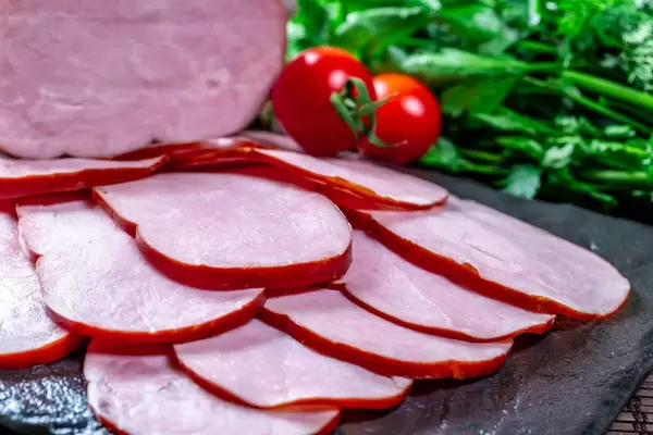 Ham with cherry tomatoes and herbs on a black stone tray