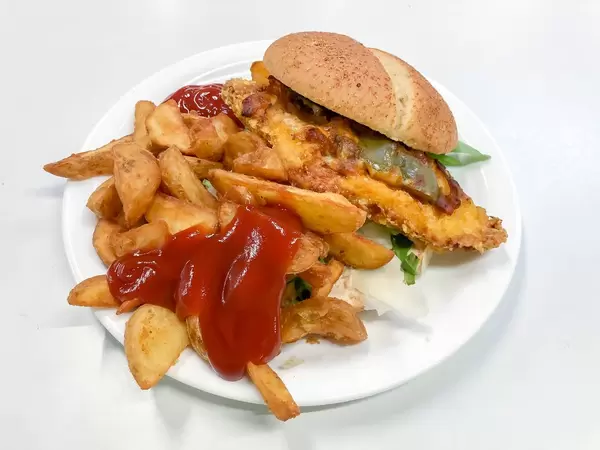 Hamburger bread filled with crispy patty, aubergine, rocket and parmesan slices, with brown baked french fries with ketchup