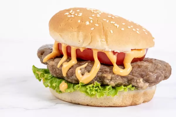 Hamburger mit zerlaufener Soße, Tomatenscheibe und Salat, auf einer weißen Oberfläche