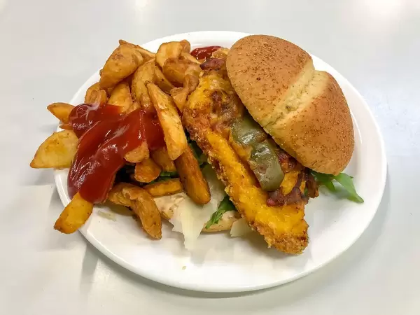 Hamburgerbrot gefüllt mit knusprigem Patty, Aubergine, Rucola und Parmesanscheiben, dazu braun gebackene Pommes Frites mit Ketchup