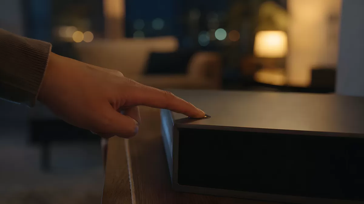 Hand berührt Knopf eines modernen Soundbars im Wohnzimmer
