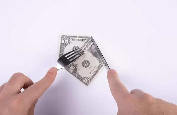 Hand cutting 100 dollar banknote with fork and knife