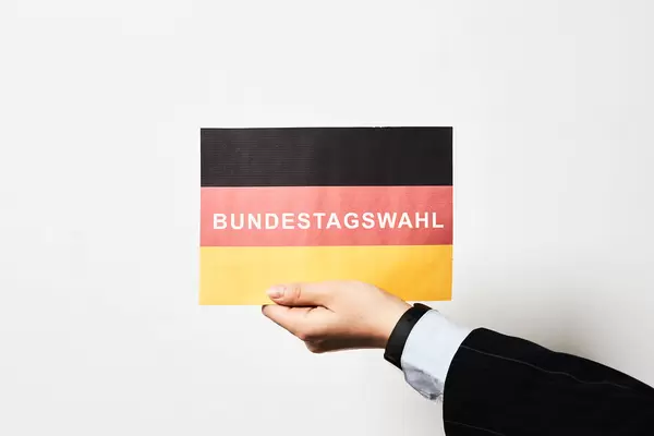 Hand eines Mannes mit Anzug und Hemd hält eine deutsche Flagge mit Schrift "Bundestagswahl"