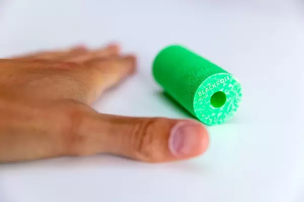 Hand eines Sportlers neben der grünen Faszienrolle von Blackroll auf weißem Untergrund, um Verspannungen zu lösen