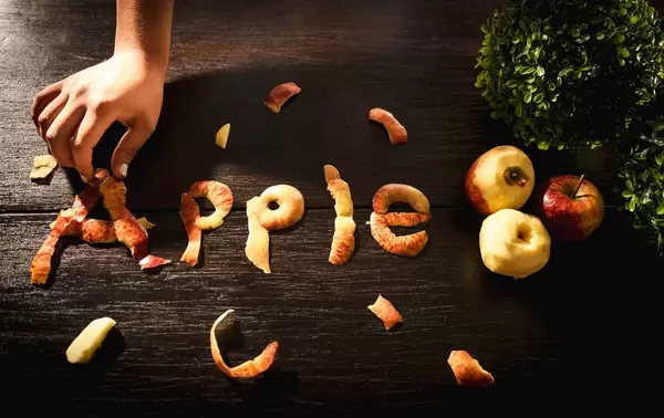 Hand forming the word APPLE with apple peel