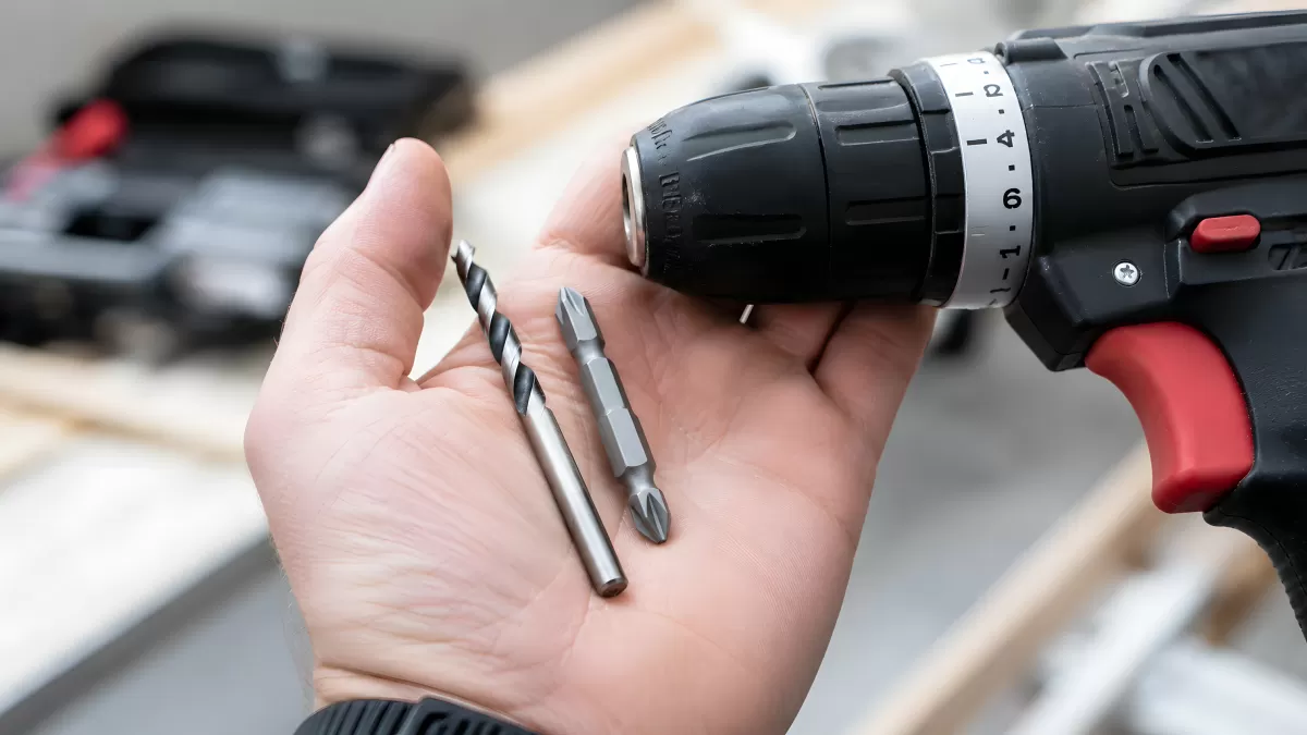 Hand hält Bohraufsätze vor einem Akkuschrauber