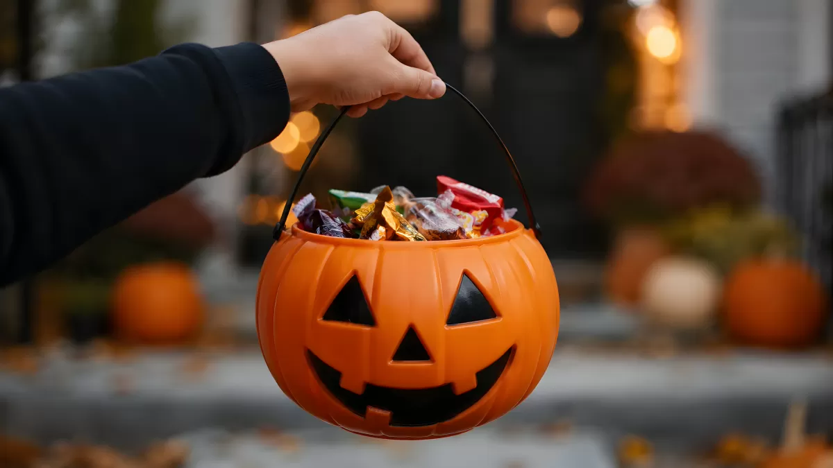 Hand hält orangefarbenen Halloween-Kürbiseimer mit Süßigkeiten