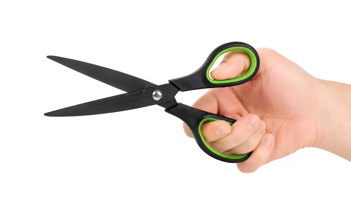 Hand hält schwarze Schere mit grünen Griffen