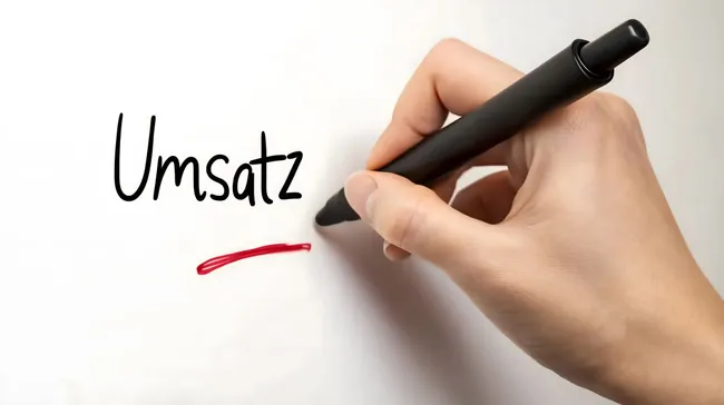 Hand hält Stift und schreibt 'Umsatz' auf Weißtafel