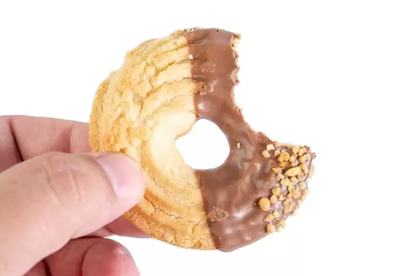 Hand hält angebissenen runden Butterkeks mit Schokoladenüberzug und Nusssplittern vor weiß
