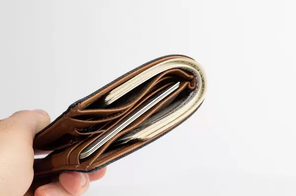 Hand hält braue Leder-Geldbörse mit Bund voller Banknoten und Kreditkarten vor weiß