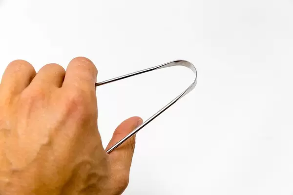 Hand hält den Edelstahl-Zungenschaber von YogaMedic vor weißem Hintergrund