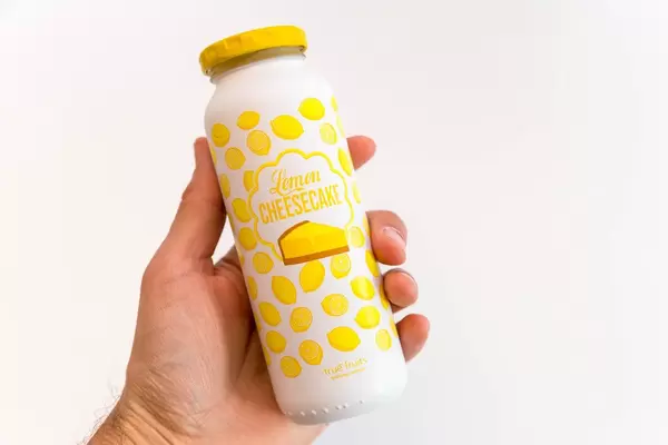 Hand hält den veganen Smoothie "Lemon Cheesecake" von True Fruits im Zitronen-Käsekuchen Geschmack und weiß-gelbem Design