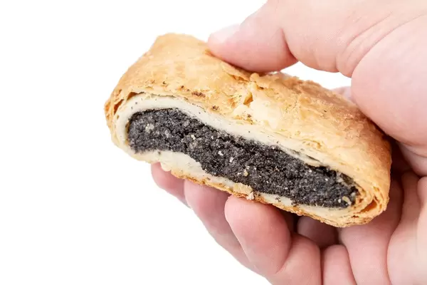 Hand hält ein abgeschnittenes Blätterteigebäck mit Mohnfüllung