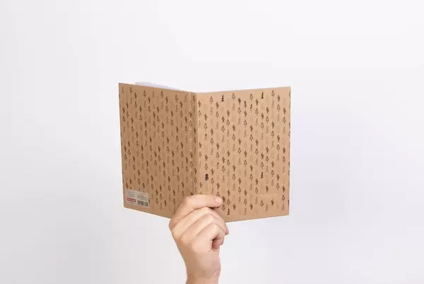 Hand hält ein Notizbuch vor weißem Hintergrund, im Naturlook