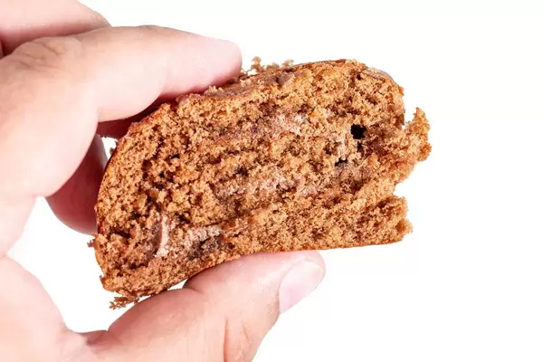 Hand hält ein Stück der Schokoladenkuchenrolle, vor weißem Hintergrund