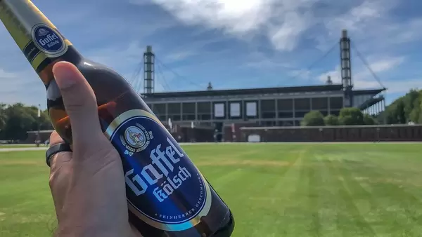 Hand hält eine Flasche Bier Gaffel Kölsch vor der Stadtwahrzeichen "RheinEnergie-Stadion"