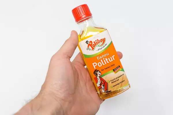 Hand hält eine Flasche fixneu Politur vor weißem Hintergrund. Die Möbelpflege für helles Holz von Poliboy