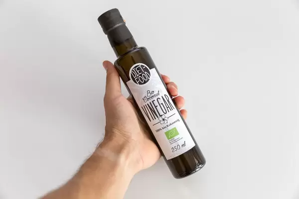 Hand hält eine schmale Flasche Bio-Kokosnuss Essig von Diet-Food