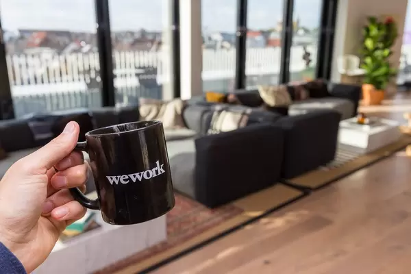 Hand hält eine schwarze WeWork-Tasse vor dem Loungebereich des modernen Gemeinschaftsbüros in der Friedensstraße in Köln