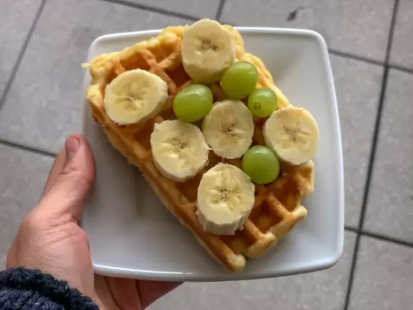 Hand hält eine Waffel mit Bananenscheiben und Weintrauben