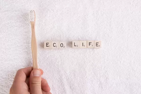 Hand hält eine Zahnbürste aus Bambus über ein weißes Handtuch, neben den Buchstabensteinen "Eco Life" / Ökologisches Leben
