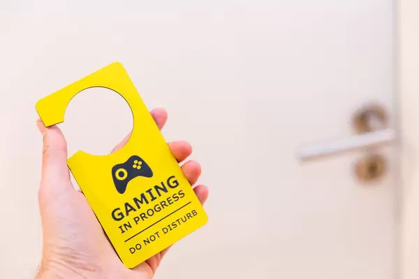 Hand hält einen gelbe Türanhänger für Zocker vor einer weißen Tür: "Ich zocke - bitte nicht stören"