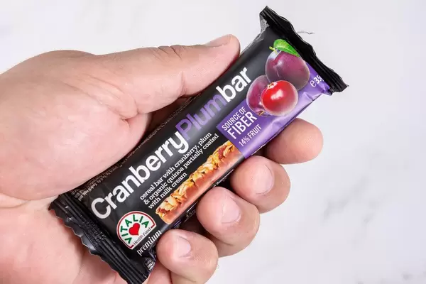 Hand hält einen gesunden Müsliriegel mit Preiselbeeren und Milchcreme, vor weißem Hintergrund