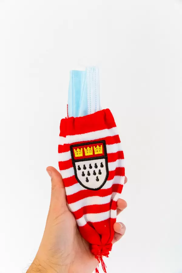 Hand hält einen Kölschglashalter mit dem Kölner Wappen in rot/weiß mit Mundschutz statt Glas