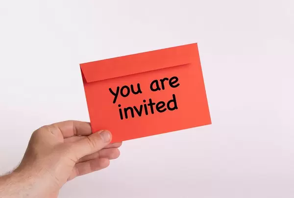 Hand hält einen roten Umschlag vor weißem Hintergrund, mit der Aufschrift "you are invited" - Du bist eingeladen