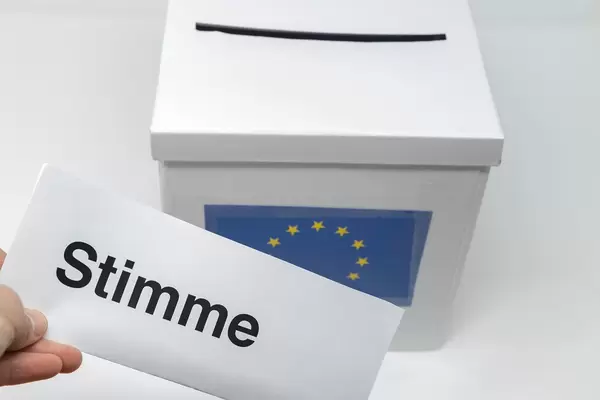 Hand hält einen Stimmzettel für die Europawahl vor einer Wahlurne, zur Abstimmung des Europäischen Parlaments der EU