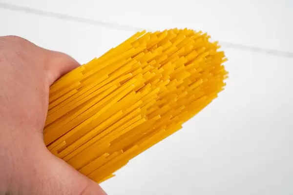 Hand hält frische, rohe Spaghetti vor einem weißen Holzhintergrund