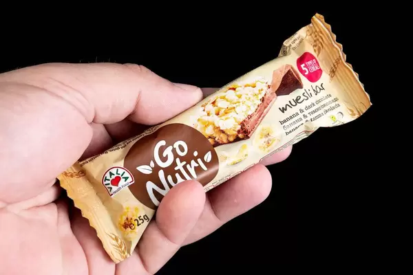 Hand hält gesunden Energieriegel mit Müsli, Getreide, Banane und dunkler Schokolade