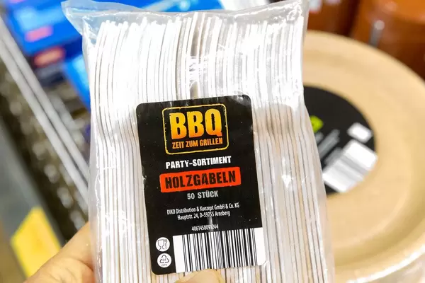 Hand hält Holzgabeln in einer Plastikverpackung, als Partyutensilien für den Grillabend