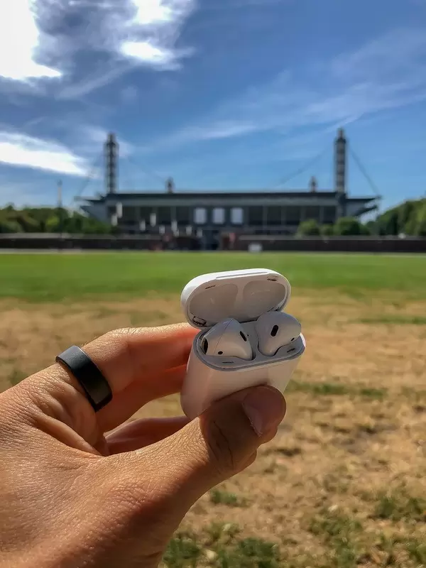 Hand hält iPhone AirPods Kopfhörer vor dem RheinEnergie Stadion in Köln