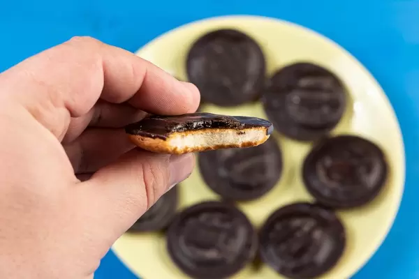Hand hält Jaffa Cake über rundem Teller mit britischem Gebäck und blauem Tisch