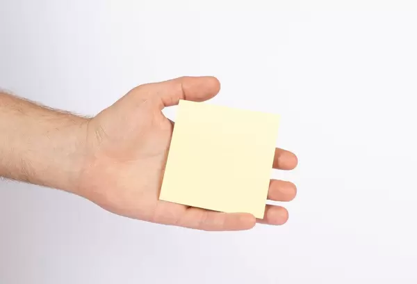 Hand hält leeres, gelbfarbenes Blatt Papier, isoliert vor weißem Hintergrund