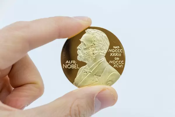 Hand hält Nobelpreis-Goldmedaille mit dem Bild von Alfred Nobel vor weißem Hintergrund