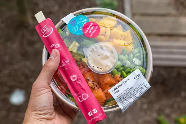 Hand hält Poké Bowl Lachs mit Essstäbchen zum Mitnehmen