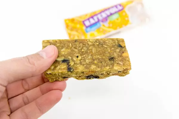 Hand hält "Hafervoll mexikanisch" Müsliriegel mit gerösteten Maiskörnern und Reismehl vor weißem Hintergrund