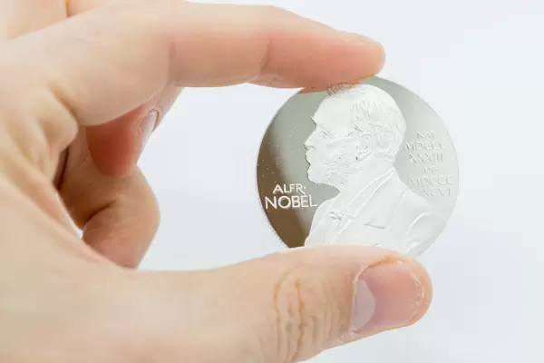 Hand hält silberne Münze mit dem Porträt von Alfred Nobel vor weißem Hintergrund