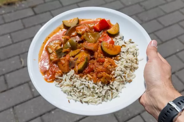Hand hält veganes Ratatouille mit Wildreis auf weißem Teller auf dem BarCamp in Koblenz