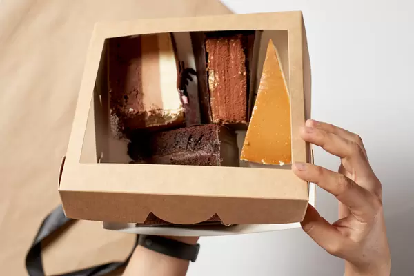 Hand hält vier Tortenstücke in einer Pappenverpackung vor weißem Hintergrund