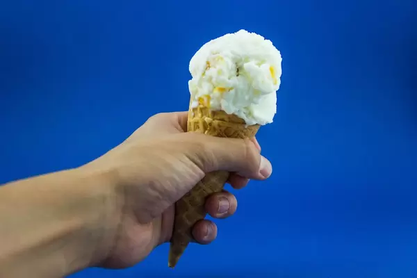 Hand hält Waffel mit Eiscreme vor blauer Wand