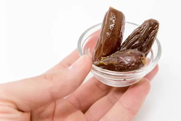 Hand hält winzige Glasschale mit drei Datteln vor weißem Hintergrund