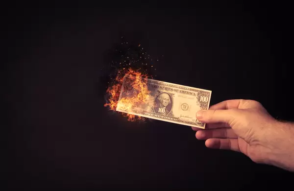 Hand holding 100 dollar banknote on fire on black bakground