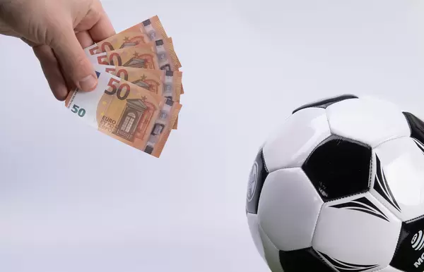 Hand holding 50 Euro banknotes and soccer ball on white background