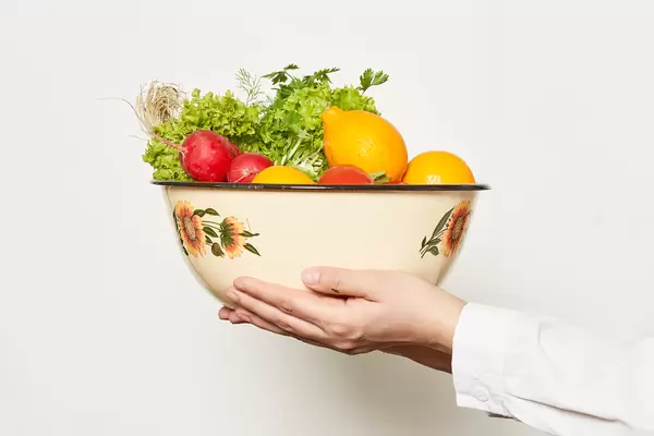 Hand holding a big bowl full with fresh fruits and vegetables