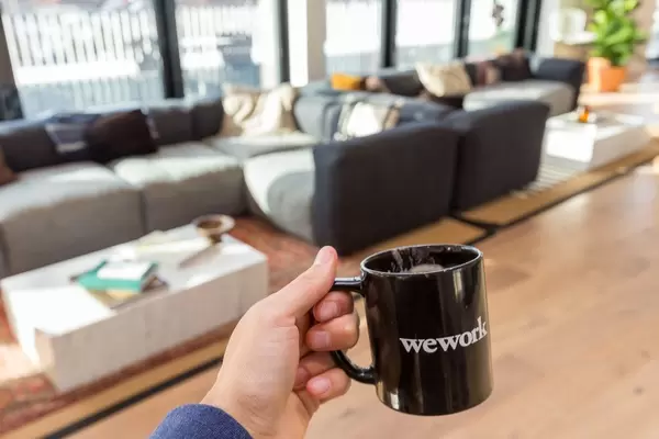 Hand holding a black WeWork cup in front of the joint lounge area of the private office spaces for rent in Cologne, Germany