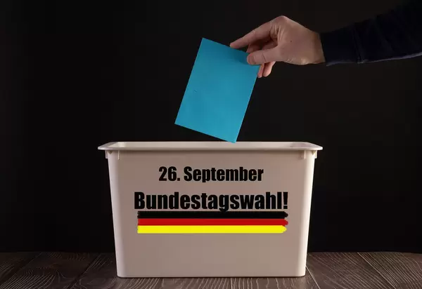 Hand holding a blue envelope over ballout box with Bundestagswahl text
